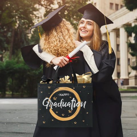 Graduates hugging with a "Happy Graduation" gift bag held in hand, showcasing Two Pack 13 Inch Graduation Gift Bags With Tissue Paper Reusable Nonwoven Gift Bags With Handles 12.8 X 10.2 X 6.3 Inch Size Perfect For Grads Class Of 2026 College High School Or 8th Grade Graduation Includes Wrapping Paper Greeting Cards And Stickers.