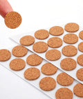 100 Piece Set Of 3/4 Inch Round Cork Furniture Pads With No Fuss Peel And Stick Backing, one pad being held above others.