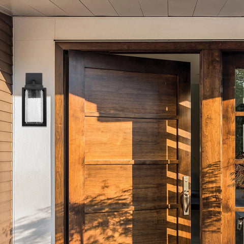 Capulet Amber Glass Center Column Outdoor Indoor Wall Sconce With LED Black Finish beside a wooden door entryway