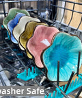 Colorful flower-shaped ceramic plates labeled as dishwasher safe displayed in a dishwasher rack.