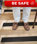 Man standing on wooden steps with Heavy Duty Anti Slip Tape For Stairs Indoor Outdoor Waterproof 4 Inch By 35 Ft Non Skid Adhesive Roll in black.
