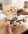 Person assembling Beginner Friendly DIY Wooden Drone Kit With Full Protective Frame on a table with tools and components.
