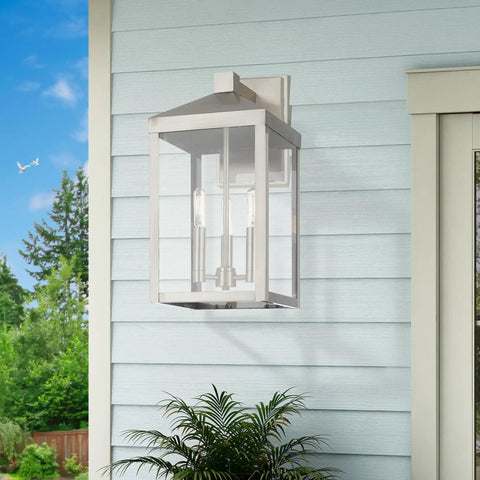 Transitional Three Light Outdoor Wall Lantern From Nyack Collection in brushed nickel on blue siding near plants