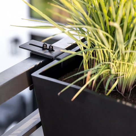 Close-up of a black plastic railing planter with adjustable brackets mounted on balcony holding plants, 36 inch long and 10 inch wide.