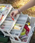 Angler organizing gear in a 3-Tray Tackle Box With Dual Top Access Dark Green Metallic And Off White Premium Tackle Storage outdoors.