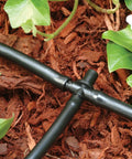 Universal 1/4 Inch Barbed Tee Fitting For Drip Irrigation installed with black tubing in a garden setting
