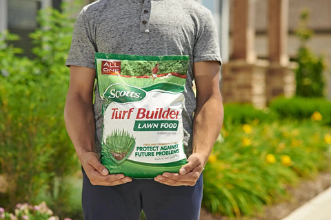 Person holding a bag of Scotts Turf Builder lawn food in a garden setting, promoting protection against future problems.