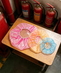 Heavy Duty Fire Alarm Dust Caps For Paint Day The 96 Piece Universal Flexible Heat Detector And Sprinkler Guard in pink, orange, and blue on a wooden table.