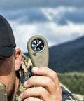 Person holding handheld wind meter with Bluetooth app connectivity for precision shooting and air flow measurement outdoors.