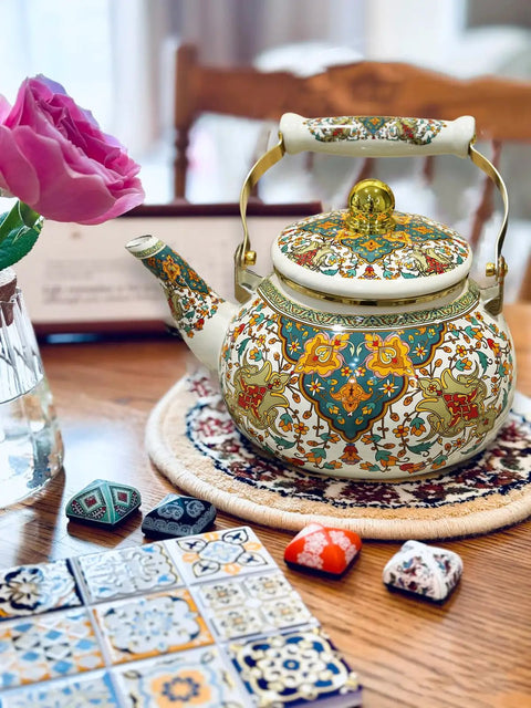 Floral Enamel Tea Kettle With Ceramic Handle Two And A Half Liter Capacity Vintage Gold Beige Boho Porcelain Teapot For Stovetop Tea Or Coffee Colorful Kitchen Decor on a table.