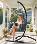 Hangin' Egg Chair With Stand, Wicker Rattan Swing Chair With 360 Degree Swivel, Cushions, Heavy Duty Iron Frame Supports Up To 330 Lbs For Indoor And Outdoor Use, Grey on porch with woman reading