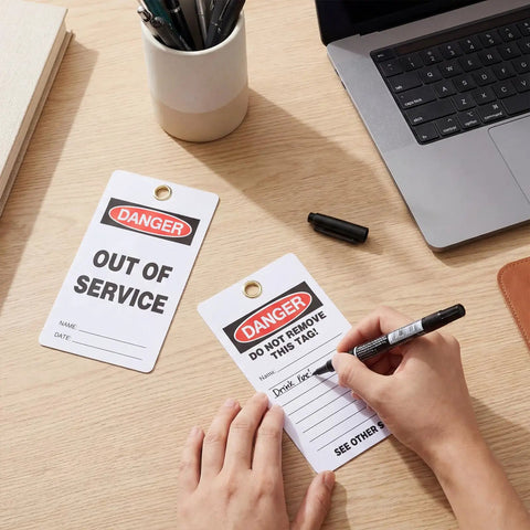 No Sweat Bulk 50 Pack Danger Out Of Service Tags For Industrial Facilities With Double Sided Bold Print and Marker Pen on a desk.