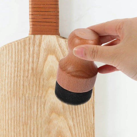Hand using the Straight Up Amazing Wooden Cutting Board Oil Brush And Built Tough Wood Wax Applicator Sponge on a light wood cutting board.