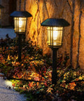 5 Pack Solar Outdoor Pathway Lights With Glass Lantern-Style Heads illuminating a garden path with a brick wall in the background