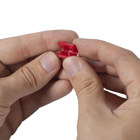 Hands separating a red GSP-24 24 Piece Twist-Apart Switch And Receptacle Spacer, showing ease of use