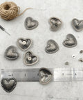 Kick Up Your Craft Game With Heart Shaped Rivets Screw Back Zinc Alloy Studs Solid Silver Metal Conchos for DIY projects arranged on a surface.