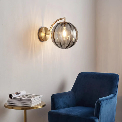Mid‑Century Modern Globe Glass Wall Sconce with Wine Red Hand‑Blown Glass, ribbed glass shade on brass arm, soft glow.