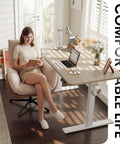 Person sitting at Electric Height Adjustable Standing Desk 48 By 24 Inches With Smooth Lift From 28.3 To 46.5 Inches, Memory Presets, Splice Desktop For Home Office, White Frame And Light Walnut Top, Sit Stand Computer Desk reading a book.