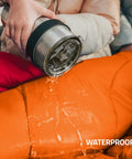 Pouring water on orange All Season Camping Sleeping Bag For Adults And Kids Lightweight Packable Water Resistant Gear For Backpacking And Hiking Easy To Carry 50 To 77 F Temperature Rating The Go To Choice For Spring Through Fall Compact And Cozy to show waterproof feature