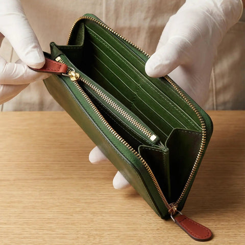 Person holding open green leather wallet with multiple compartments and gold zipper.