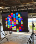 Colorful illuminated display panel hanging with truss setup in a workshop with garage background.