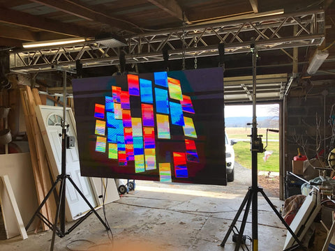Colorful illuminated display panel hanging with truss setup in a workshop with garage background.