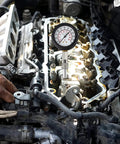 Compression tester gauge installed on car engine cylinder head; black case, white dial, metal probe