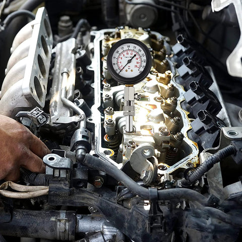 Compression tester gauge installed on car engine cylinder head; black case, white dial, metal probe