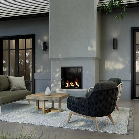 Outdoor patio scene with 5 Inch Cylinder Outdoor LED Wall Sconce with 2 Lights Up and Down mounted beside a modern fireplace.