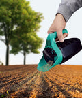 Hand holding All Season Handy Seed Spreader For Lawn Care Pro Grade Adjustable Grass Seed And Fertilizer Spreader over soil.