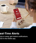 Person holding a smartphone displaying real-time CO alerts, part of the Smart Carbon Monoxide Detector With Plug In Design And AA Battery Backup.