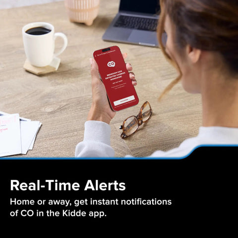 Person holding a smartphone displaying real-time CO alerts, part of the Smart Carbon Monoxide Detector With Plug In Design And AA Battery Backup.