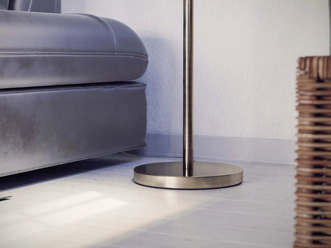 Base of the Edison Floor Lamp In Antique Brass Finish beside a sofa, highlighting metal construction and rustic vibe.