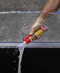 Side view of a hand squeezing 9 oz Flex Caulk white sealant from a red-capped tube onto a clear panel edge.