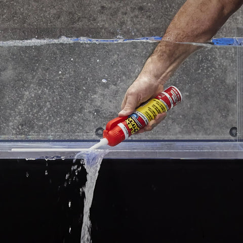 Side view of a hand squeezing 9 oz Flex Caulk white sealant from a red-capped tube onto a clear panel edge.