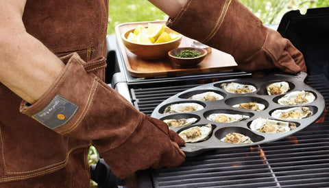 Person grilling oysters on a cast iron oyster grill pan with 12 cavities on a barbecue, showcasing nonstick surface in use.