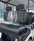 White Eight Passenger Electric Golf Cart Rolled Up Tight With Beefy Dual Arm Suspensions Silky Smooth Five Kilowatt Motor Plus Touchscreen Audio And Deep Reclining Lounge Seats featuring black diamond-stitched lounge seats.