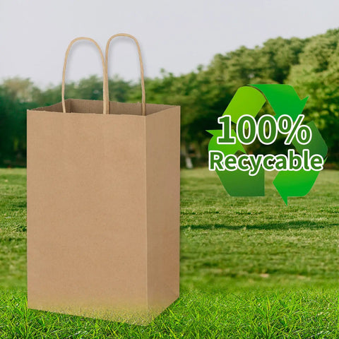 Bulk Brown Kraft Paper Bags With Handles 100 Pack Small Gift Bags 5.25 By 3.25 By 8.25 Inches Durable 110 Gsm Heavy Duty, shown on grass with recycle icon