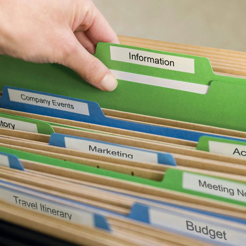 Hand reaching for green labeled file marked 'Information' among colorful folders for organized filing.