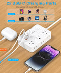 Heavy Duty Surge Protector Power Strip With Six Separated AC Outlets And Dual USB C Plus Dual USB A Ports Five Foot Extension Cord Plug And Play Design For No Fuss Multidevice Charging on wooden table with phone charging.