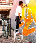 Heavy Duty Metal Spray Paint Storage Rack Eight Tier Lube Can Organizer with paint cans in use beside artist painting a wall.