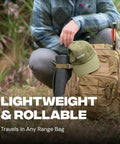 Person carrying a khaki backpack with attached rolled-up mat and cap in outdoor setting, highlighting portability and utility.