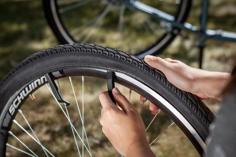 Using Deluxe Bike Tube Repair Kit With Tire Patches, Levers, Scuffer And Tools to remove a bike tire on grass.