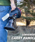 Person holding Little Buddy Portable Radiant Propane Heater, convenient carry handle visible, outdoors in a wooded area.