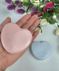 Compact Travel Sewing Kit Two Pack Featuring Adorable Heart Shaped Cases Pink And Blue held in hand with flowers in background.