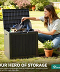 Woman placing items into 30 Gallon Outdoor Storage Deck Box Made From Waterproof Resin With Lockable Lid For Cushions Pool Accessories And Garden Tools A Versatile Patio Table All In One Go To Storage Ottoman For Indoor Or Outdoor Use.