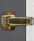 Built Tough Spring Loaded Screen Door Catch Slick Brass Finish Iron Frame close-up, mounted for secure entryway locking.
