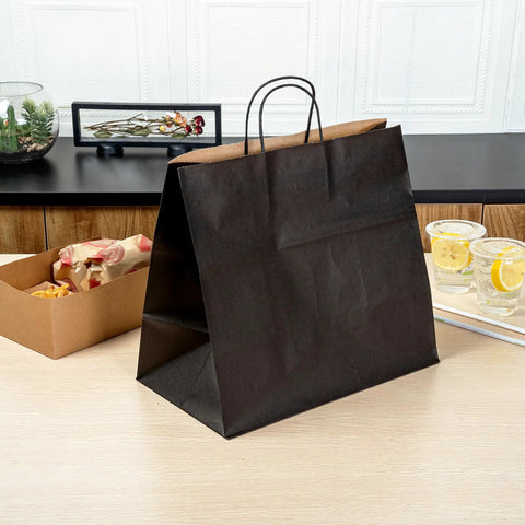 Black kraft paper bag with handles on table, from 100 Pack Stand Open Paper Shopping Bags With Handles For Grab And Go Takeout And Retail Durable Kraft Paper Carrier Bags 14.17 X 8.26 X 13.19 Inches Easy Carry Totes For Gifts Groceries And Everyday Shop Runs.
