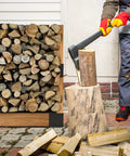 Person chopping firewood with an axe next to a stacked woodpile outdoors.