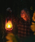 Person holding a glowing 12 Inch Hurricane Lantern With Durable Red Finish For Camping And Emergencies outdoors at night.